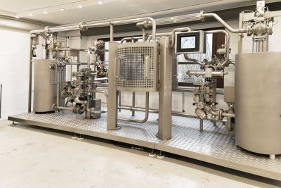Industrielle Demonstrationsanlage mit mehreren Edelstahltanks, einem komplexen Rohrleitungssystem mit Ventilen und Armaturen sowie einem Touchscreen-Bedienfeld; die Anlage steht in einem hellen Raum mit strukturiertem Bodengitter und zeigt ein vollst&auml;ndiges Molchsystem zur Prozessoptimierung.