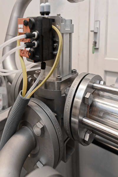 Nahaufnahme eines industriellen Verteilknotens mit Edelstahlrohren, einem pneumatischen Ventil und transparenten Leitungen, die mit einem Steuerungsmodul verbunden sind; die Komponenten sind Teil eines Demonstrationssystems.