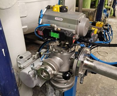 Una válvula industrial compleja con múltiples actuadores, válvulas y conexiones eléctricas conectadas a un sistema de tuberías. Los componentes son metálicos, con detalles en azul y amarillo provenientes de los cables y válvulas.